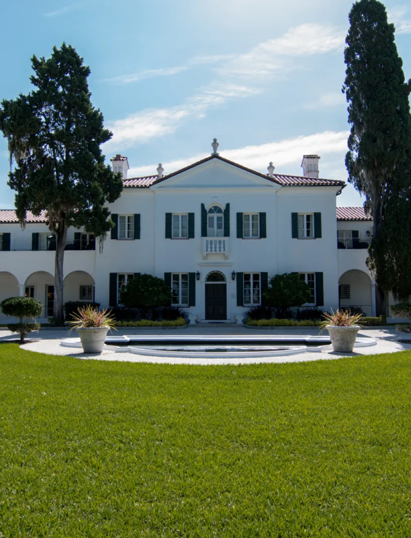 The Crane Cottage at Jekyll Island Club Hotel, with its white Mediterranean Revival style facade, red-tile roof, and a central cypress tree against a blue sky.