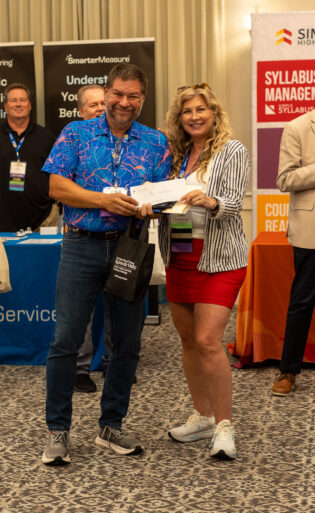 A woman and man pose with a check as people smile in the background.