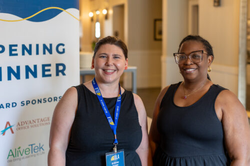 Two smiling women stand in front of an “Opening Dinner Award Sponsors” banner.