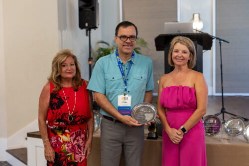 Two women stand next to a man holding a DLA award.