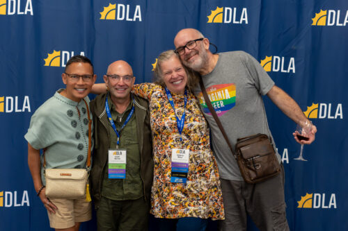 Three men and a woman stand, smiling in front of a DLA backdrop.