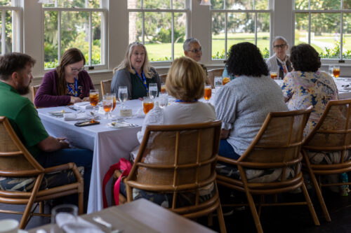 A group of people converse at a table with a window view.