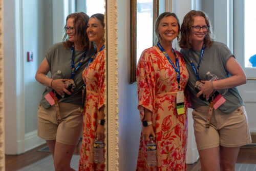 Two women pose, smiling beside a mirror.