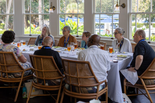 A group of people converse at a table with a window view.
