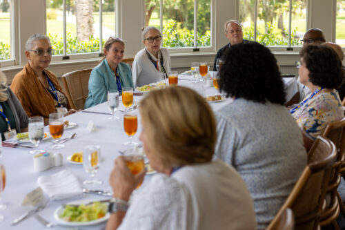 A group of people converse at a table with a window view.