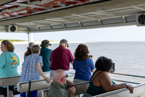 People overlook the boat’s railing to take pictures of the body of water.
