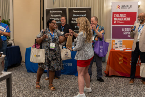 A woman hands another woman a bag as people smile and clap in the background.