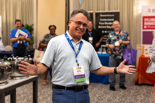 Standing in front of booths, a man wearing a DLA lanyard smiles at the camera.