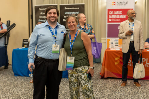 Standing in front of booths, a man and woman wearing DLA lanyards smile at the camera.