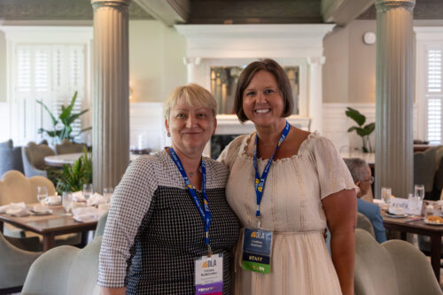 Two women smile at the camera in an elegant dining room.